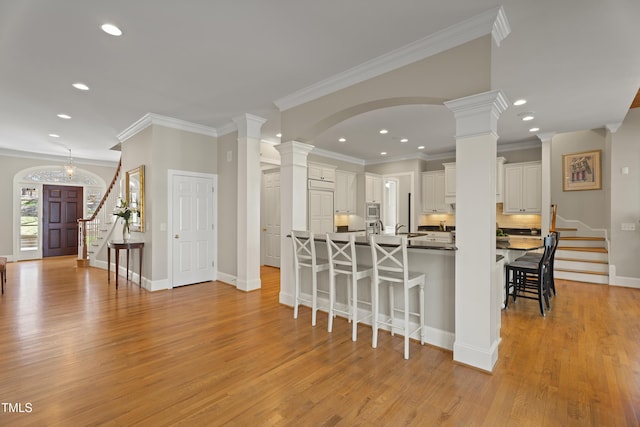 kitchen with decorative columns, recessed lighting, stainless steel microwave, light wood-style flooring, and a kitchen bar