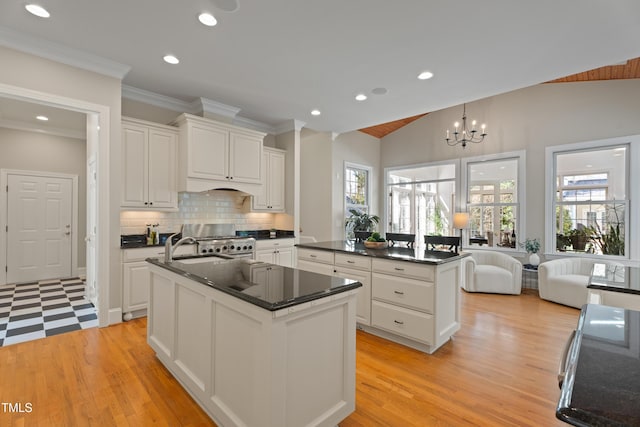 kitchen with vaulted ceiling, white cabinets, a kitchen island with sink, and plenty of natural light