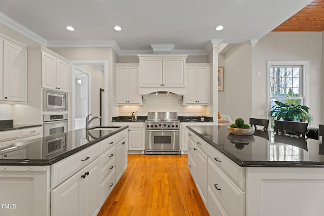 kitchen featuring light wood finished floors, stainless steel appliances, white cabinets, a sink, and an island with sink