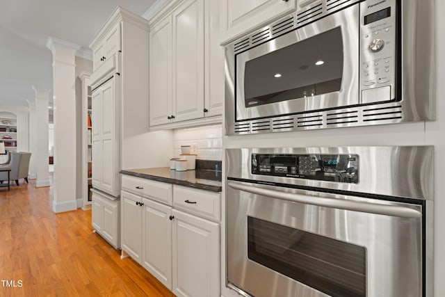 kitchen featuring light wood finished floors, decorative columns, appliances with stainless steel finishes, and white cabinets