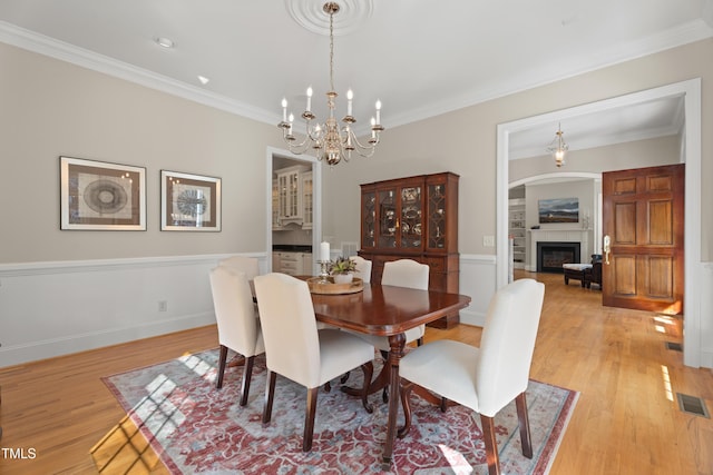 dining space with light wood-style floors, a glass covered fireplace, visible vents, and crown molding