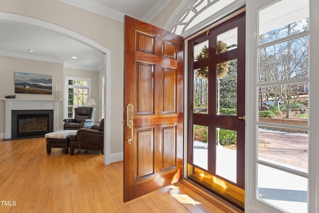 entryway with light wood finished floors, arched walkways, a glass covered fireplace, and ornamental molding