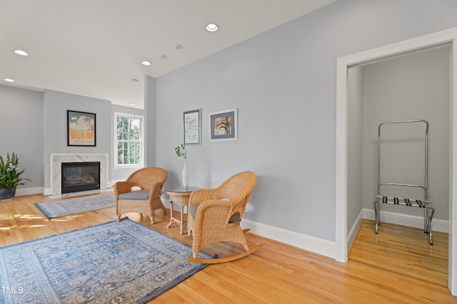 sitting room featuring a high end fireplace, light wood-style flooring, and baseboards