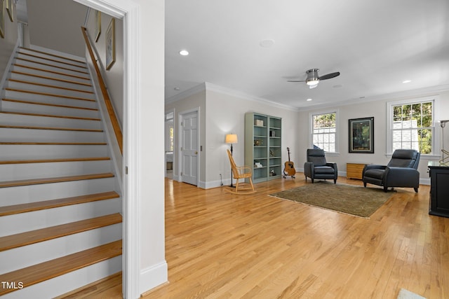 living room featuring baseboards, crown molding, light wood finished floors, and stairs