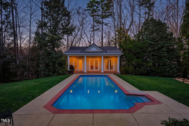 pool at dusk featuring a yard, french doors, a patio area, and an outdoor pool