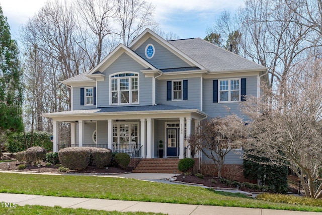 view of front of house featuring covered porch, a shingled roof, a front yard, and brick siding