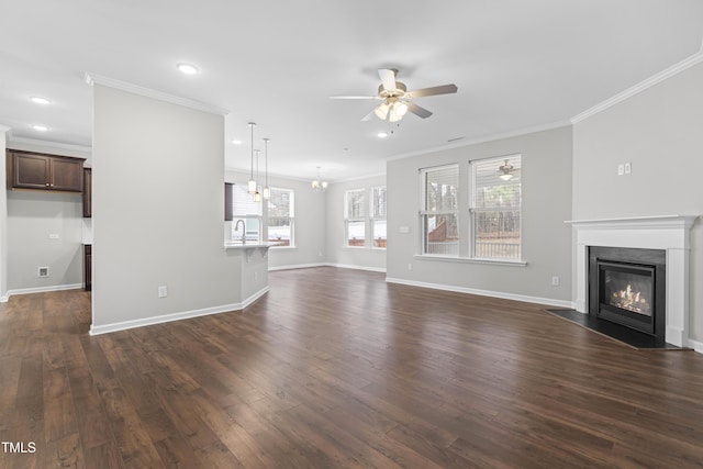 unfurnished living room with dark wood-type flooring, baseboards, a fireplace with flush hearth, ornamental molding, and ceiling fan with notable chandelier