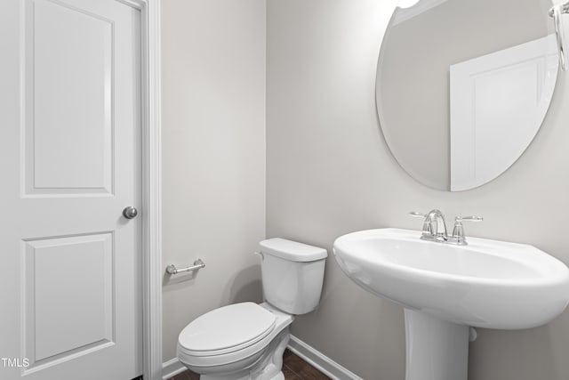 bathroom with toilet, wood finished floors, baseboards, and a sink