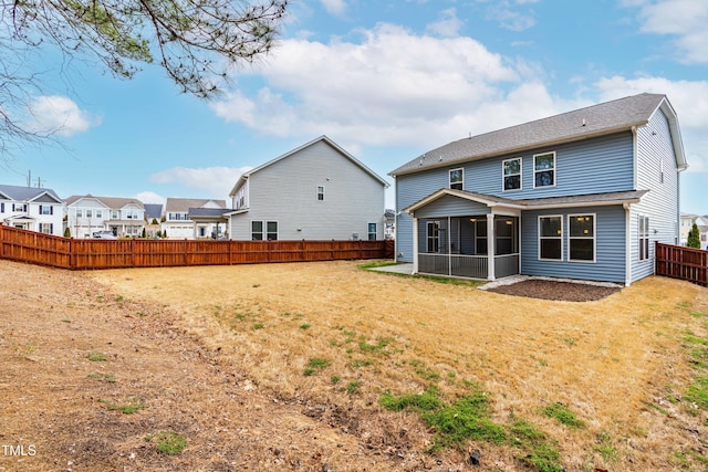 rear view of property featuring a fenced backyard, a yard, a residential view, roof with shingles, and a sunroom