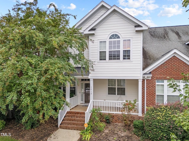 traditional home with a shingled roof, covered porch, and brick siding