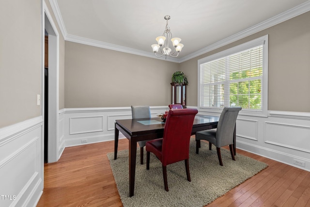 dining space featuring crown molding, light wood finished floors, wainscoting, and an inviting chandelier