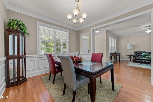 dining space with a wainscoted wall, crown molding, a decorative wall, an inviting chandelier, and light wood-type flooring