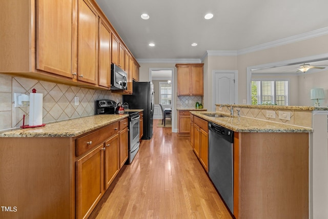 kitchen with appliances with stainless steel finishes, light stone countertops, crown molding, light wood-type flooring, and a sink