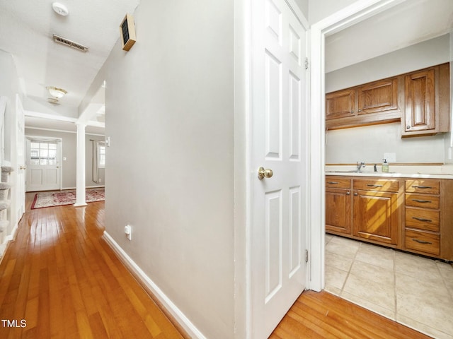 hall with decorative columns, visible vents, light wood-style floors, a sink, and baseboards