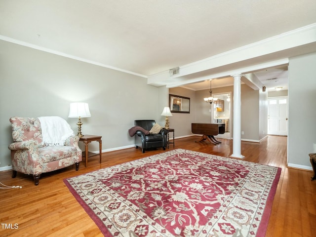 sitting room with crown molding, ornate columns, hardwood / wood-style floors, an inviting chandelier, and baseboards