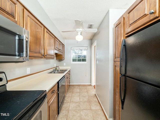 kitchen featuring a textured ceiling, light tile patterned floors, a sink, appliances with stainless steel finishes, and brown cabinetry