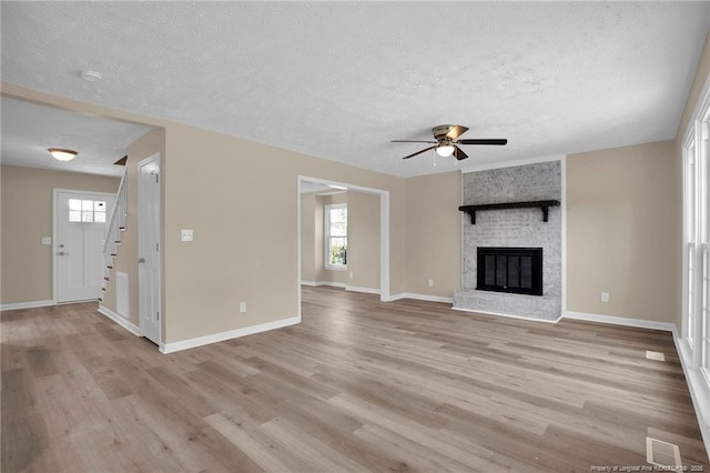 unfurnished living room featuring light wood finished floors, a brick fireplace, and a healthy amount of sunlight