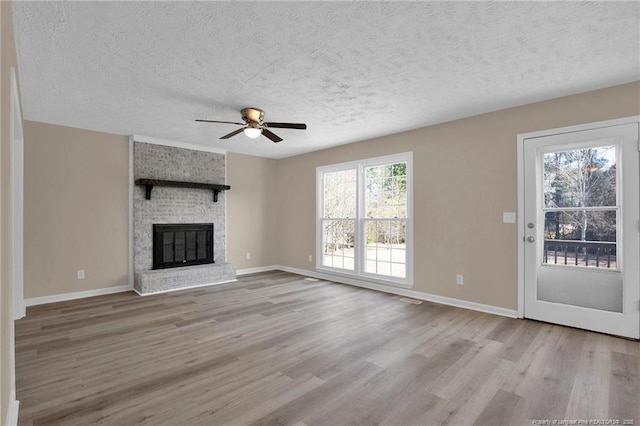 unfurnished living room with a textured ceiling, a fireplace, baseboards, and wood finished floors