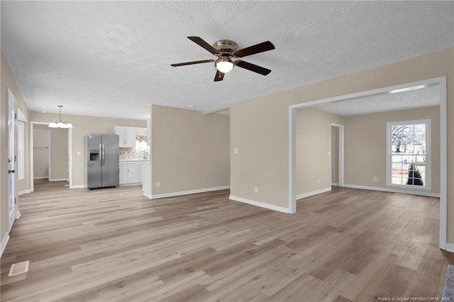 unfurnished living room with a textured ceiling, light wood-style flooring, ceiling fan with notable chandelier, visible vents, and baseboards