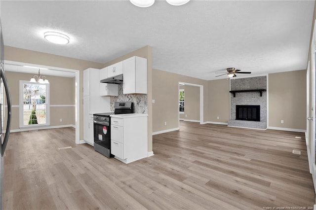 kitchen featuring under cabinet range hood, a fireplace, white cabinets, decorative backsplash, and stainless steel electric range oven