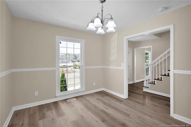 unfurnished dining area featuring baseboards, visible vents, wood finished floors, an inviting chandelier, and stairs