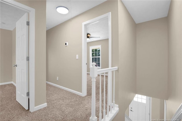 hallway featuring carpet floors, baseboards, and an upstairs landing