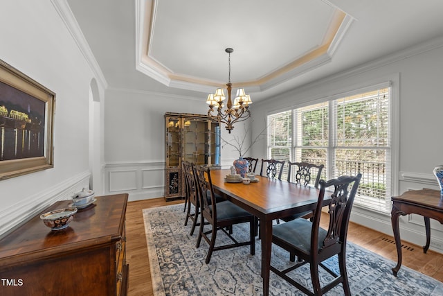 dining space with wood finished floors, a wainscoted wall, a tray ceiling, a decorative wall, and a chandelier