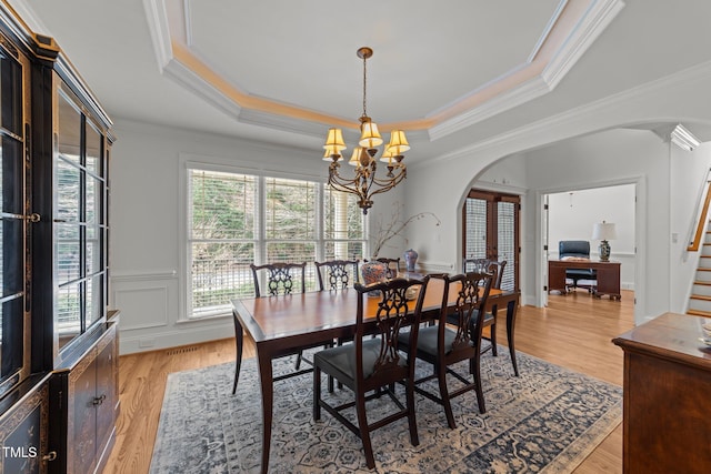 dining space featuring a notable chandelier, light wood-style flooring, a tray ceiling, arched walkways, and stairs