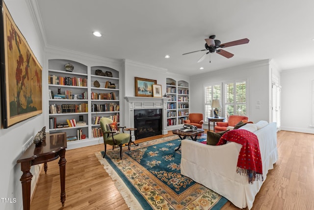 living room featuring a fireplace with flush hearth, ornamental molding, ceiling fan, and wood finished floors