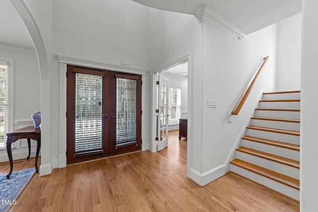 entrance foyer featuring baseboards, arched walkways, stairs, french doors, and light wood-type flooring