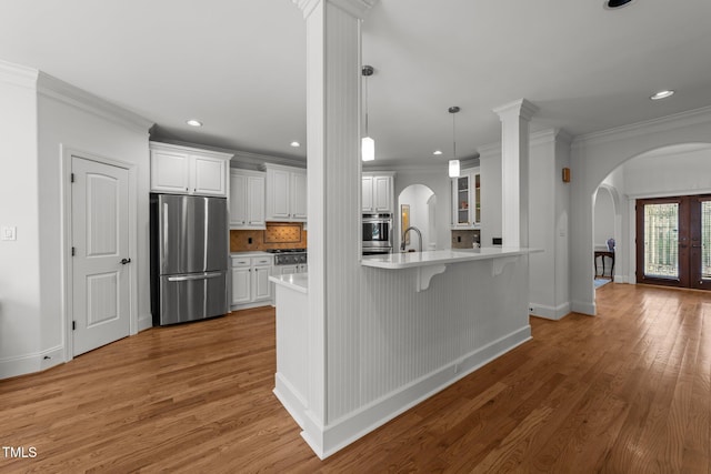 kitchen featuring a breakfast bar, light countertops, light wood-style flooring, appliances with stainless steel finishes, and arched walkways