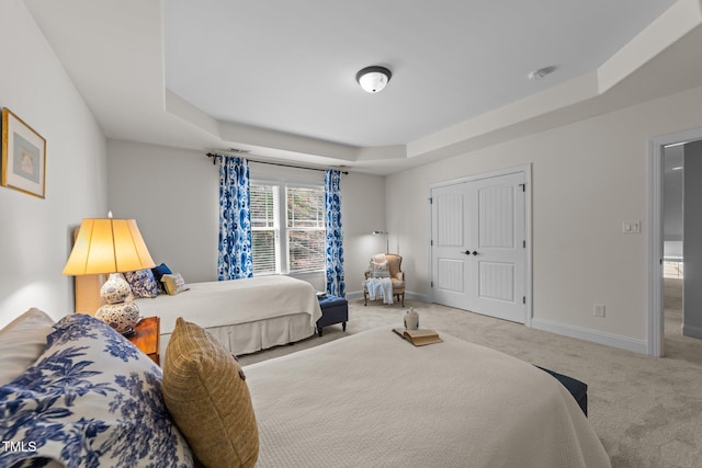 bedroom featuring a raised ceiling, a closet, baseboards, and carpet floors