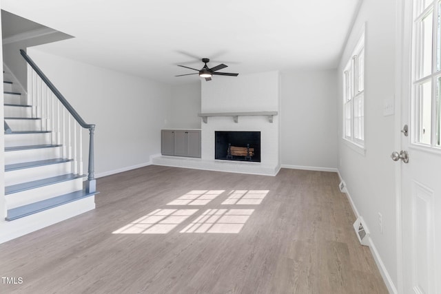 unfurnished living room featuring a fireplace, visible vents, stairway, ceiling fan, and wood finished floors