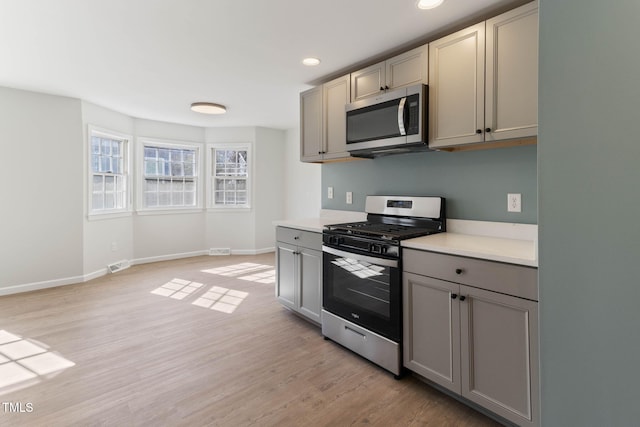 kitchen featuring baseboards, appliances with stainless steel finishes, light countertops, gray cabinetry, and light wood-type flooring