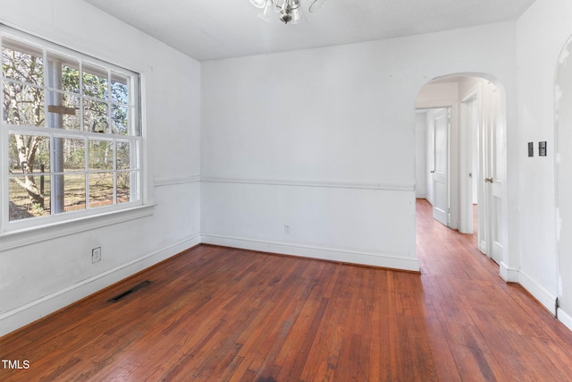 empty room featuring arched walkways, visible vents, baseboards, and hardwood / wood-style flooring