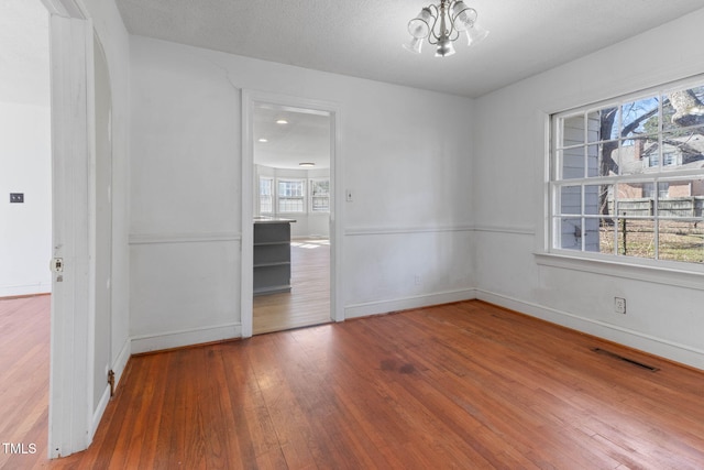 unfurnished room with arched walkways, a wealth of natural light, hardwood / wood-style flooring, and visible vents