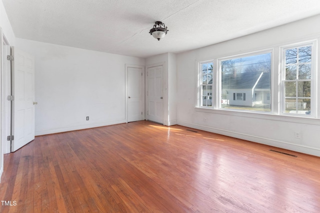 unfurnished bedroom with wood-type flooring, a textured ceiling, visible vents, and baseboards