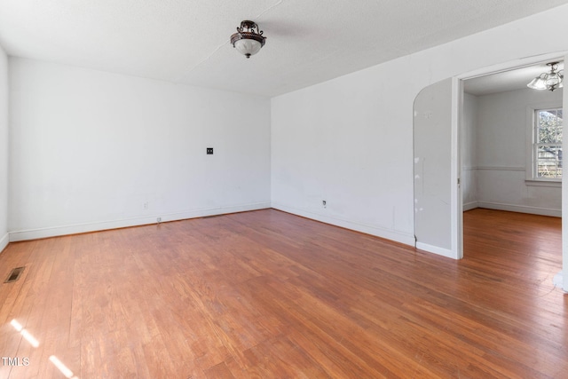 unfurnished room with baseboards, visible vents, arched walkways, and wood finished floors