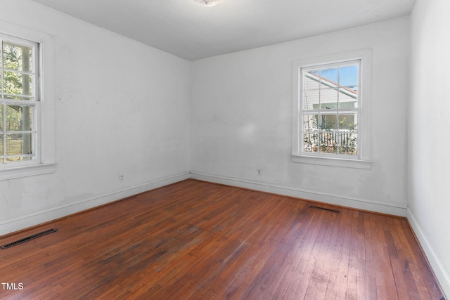 spare room with a healthy amount of sunlight, visible vents, and hardwood / wood-style floors