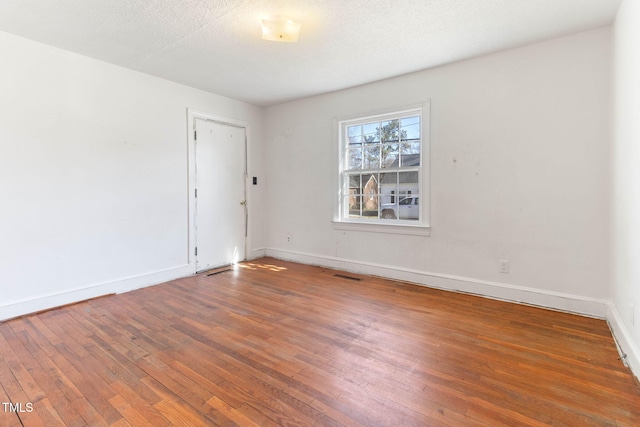 spare room with a textured ceiling, hardwood / wood-style floors, visible vents, and baseboards