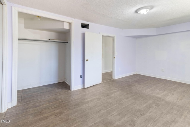 unfurnished bedroom with a closet, visible vents, a textured ceiling, and wood finished floors