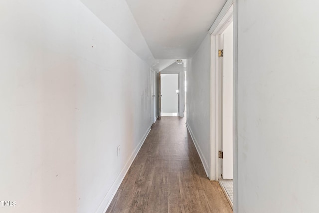 hallway featuring lofted ceiling, wood finished floors, and baseboards