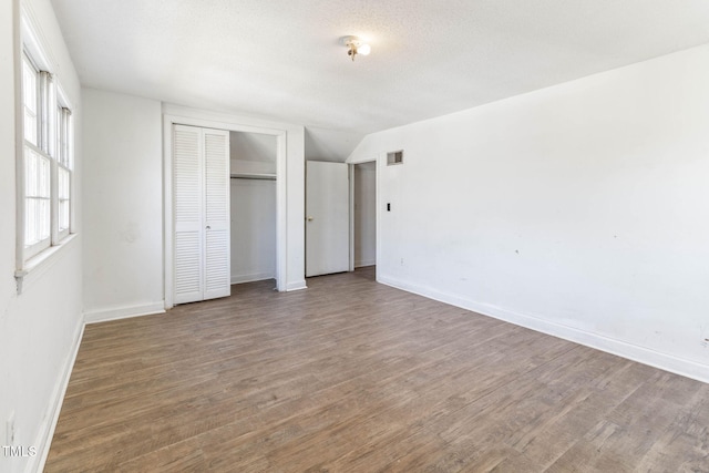 unfurnished bedroom with a closet, visible vents, baseboards, and wood finished floors