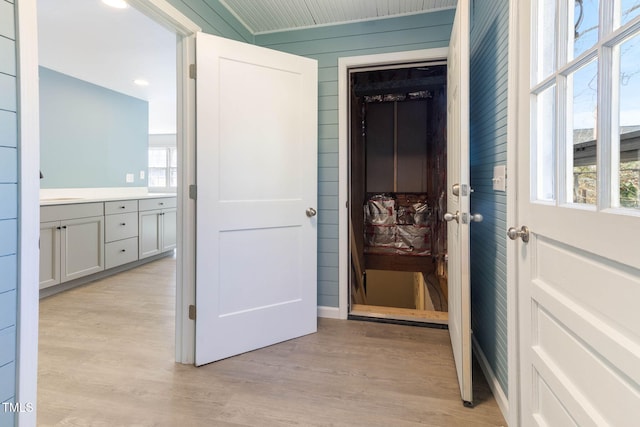 hallway with light wood-type flooring and wooden walls