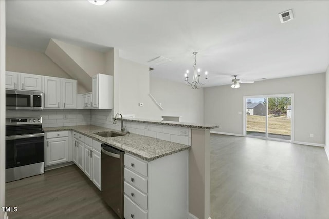 kitchen with tasteful backsplash, appliances with stainless steel finishes, light stone counters, a peninsula, and a sink