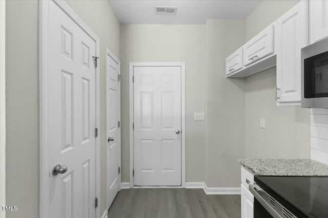 kitchen with dark wood-type flooring, stainless steel microwave, visible vents, and white cabinetry