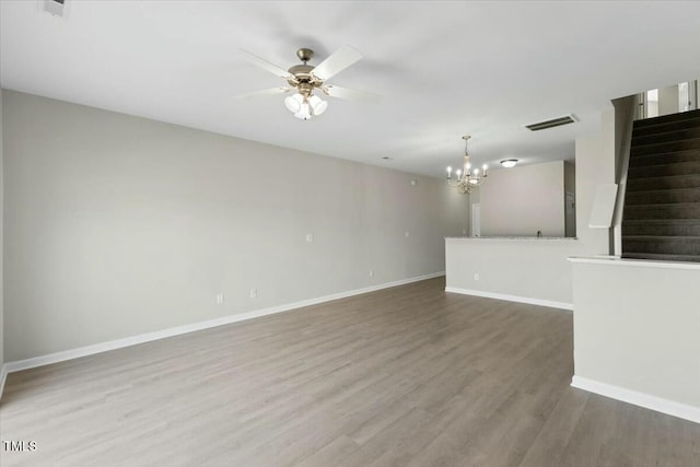 spare room with ceiling fan with notable chandelier, wood finished floors, visible vents, baseboards, and stairway