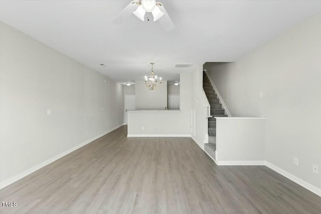 unfurnished living room with baseboards, visible vents, wood finished floors, stairs, and ceiling fan with notable chandelier