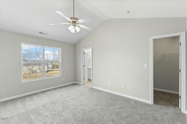 unfurnished bedroom featuring carpet floors, lofted ceiling, visible vents, a spacious closet, and baseboards