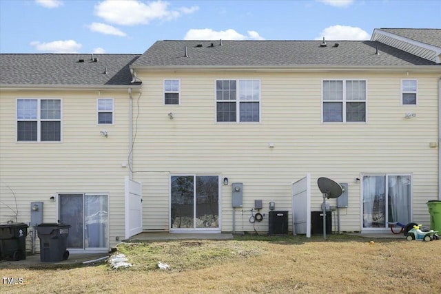 rear view of property with a shingled roof and a lawn